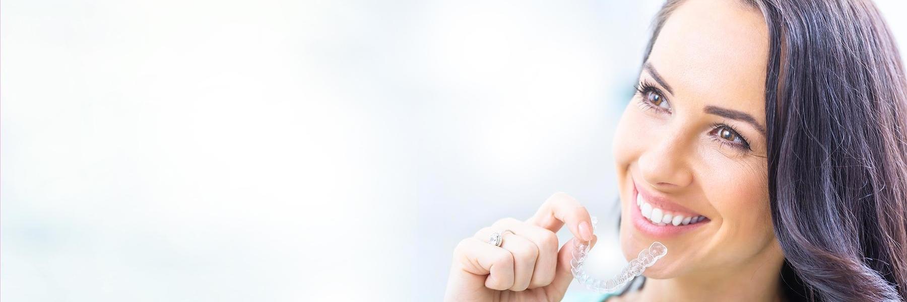 woman smiling while holding clear aligners in Johnston