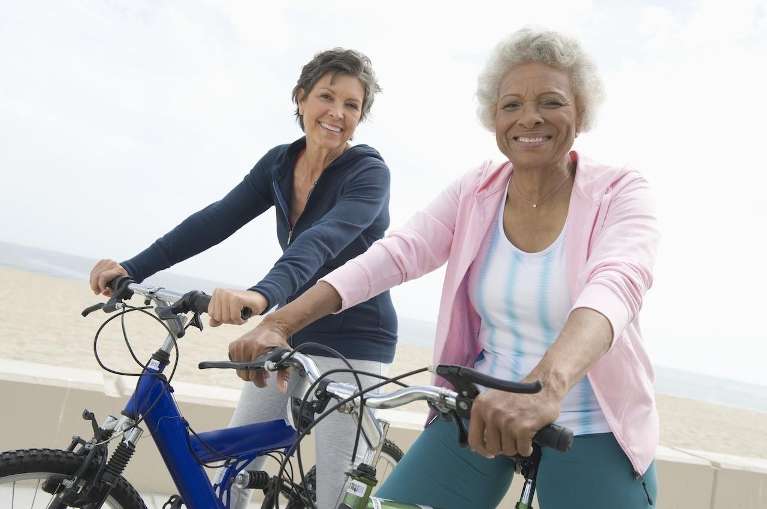 Smiling older women biking on the beach, enjoying life with dental bridges.