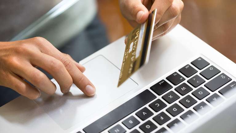 close up of person's hands while using a laptop and holding a credit card