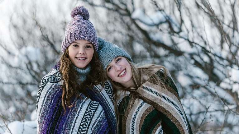 Two smiling teenage girls in winter hats outdoors, showing healthy teeth and braces in Urbandale IA