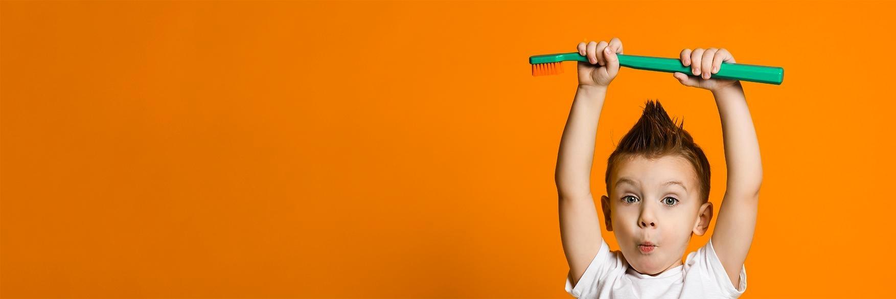 young boy holding a large toothbrush above his head in Johnston