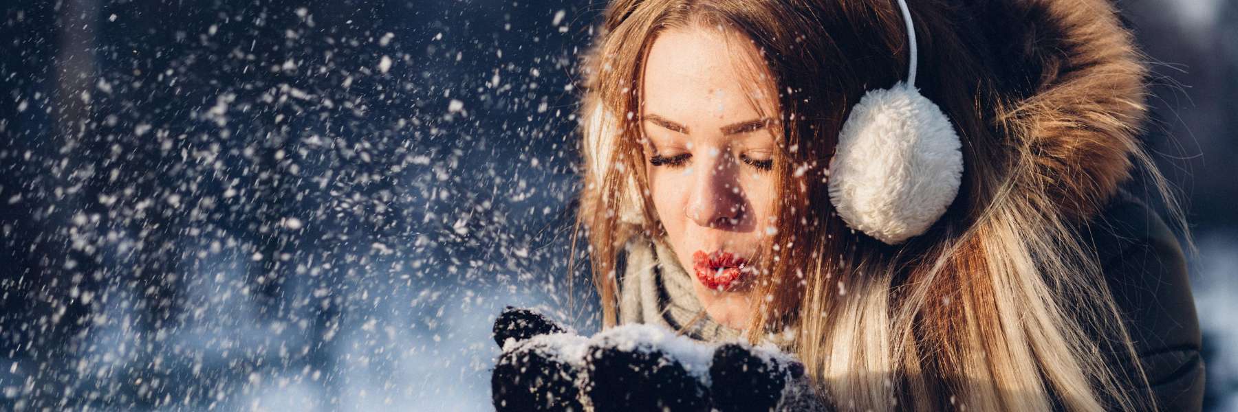 Young woman in earmuffs blowing snow outdoors on a cold winter day in Urbandale IA